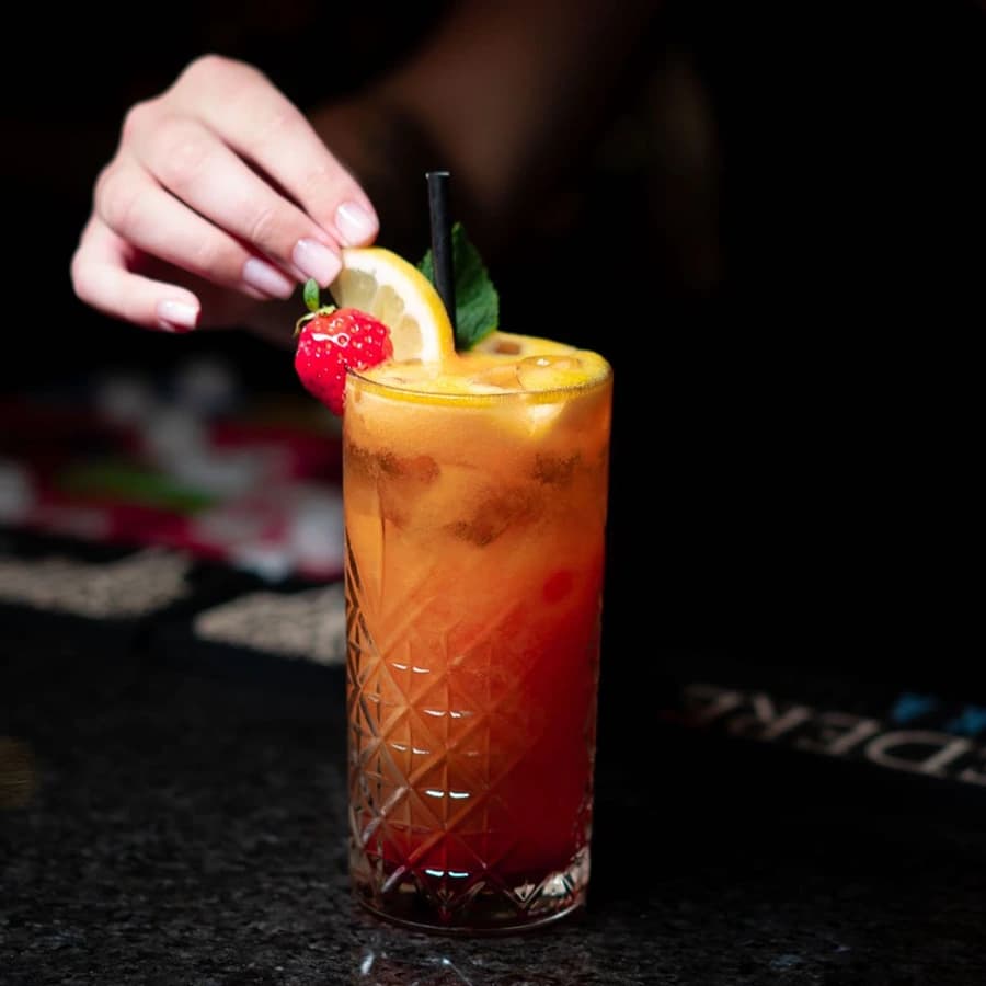 A tall citrus cocktail being garnished with a slice of orange