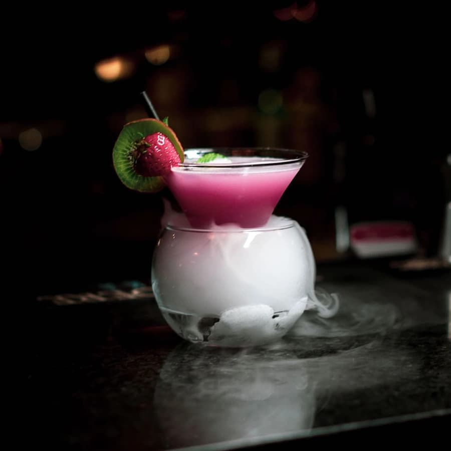 A pink cocktail in a frosted glass with dry-ice vapour spilling over the rim