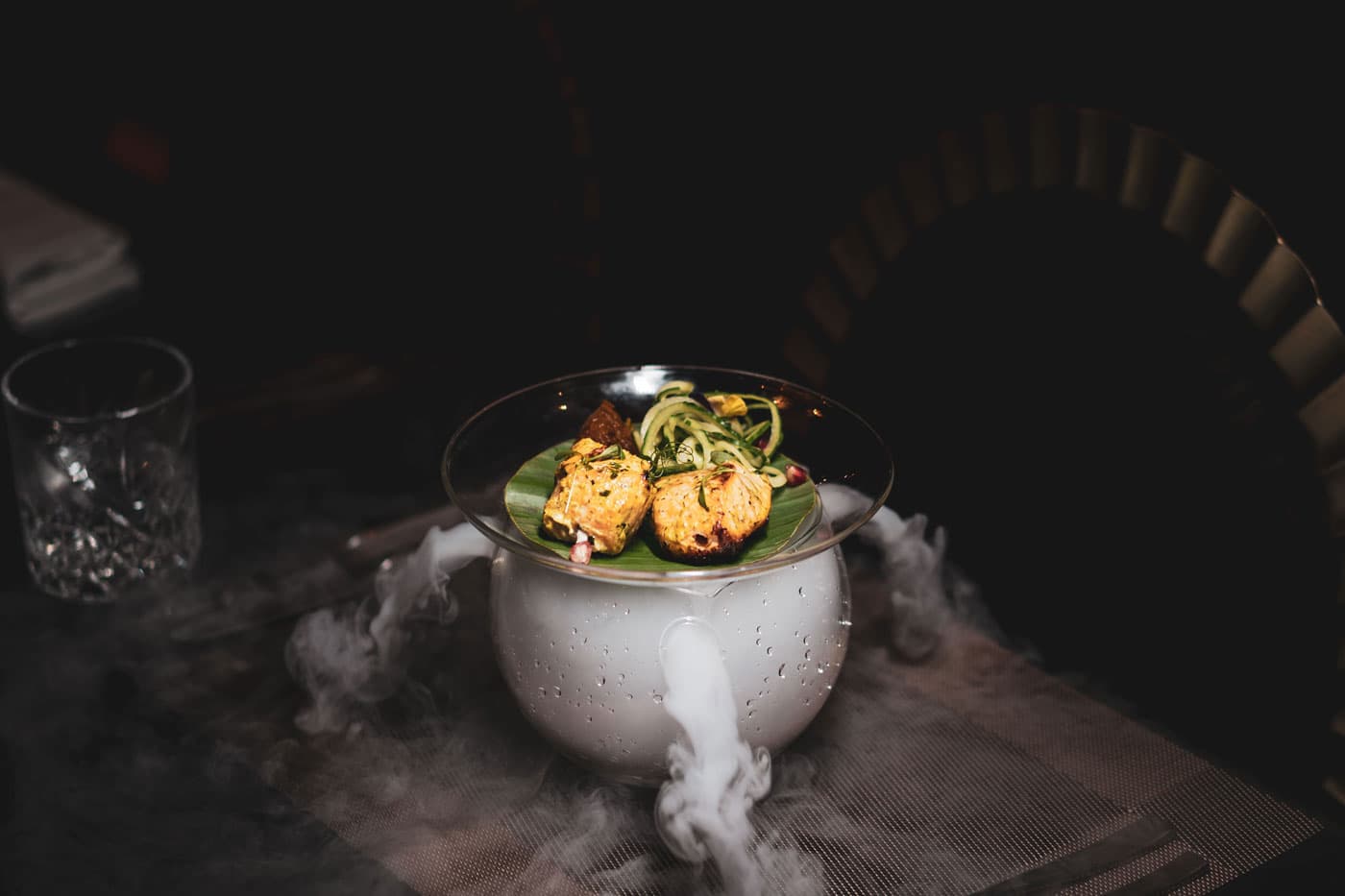 A dessert served in a white bowl surrounded by dry-ice vapour