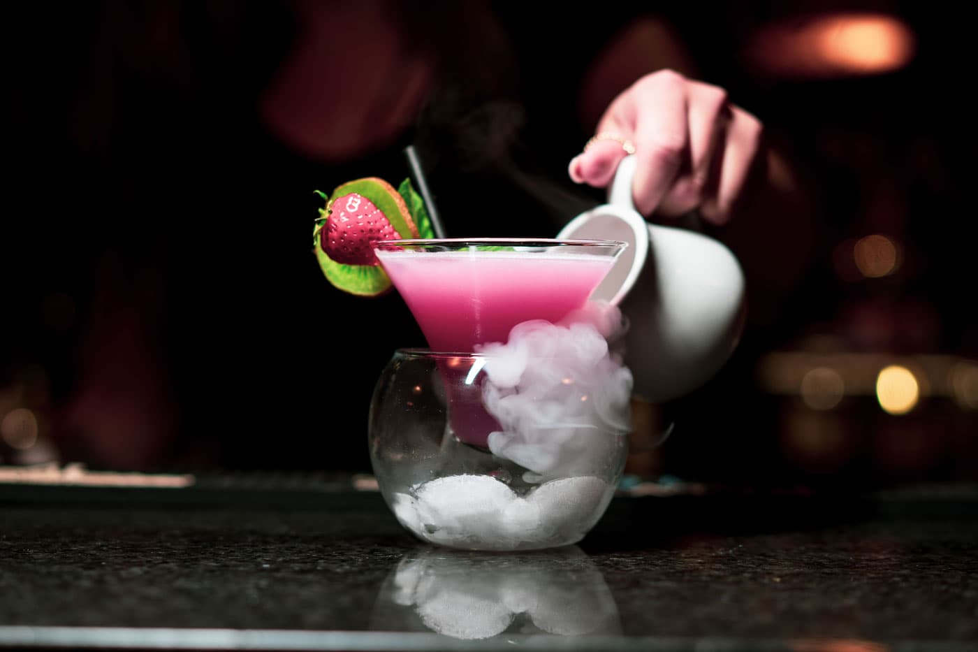 A bartender garnishing a pink cocktail served over dry-ice vapour