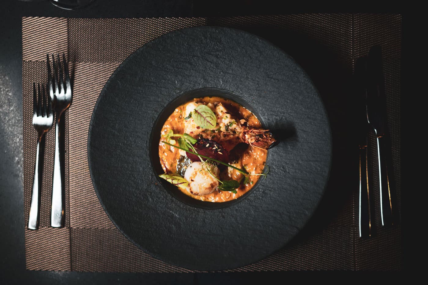 A seafood starter in a shallow black bowl, laid with cutlery on a dark table
