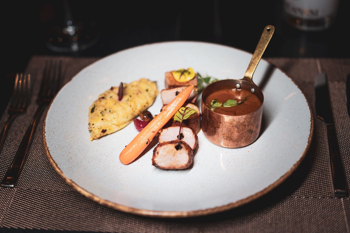 Seared meat with a copper pot of curry sauce and roasted carrot on a pale plate