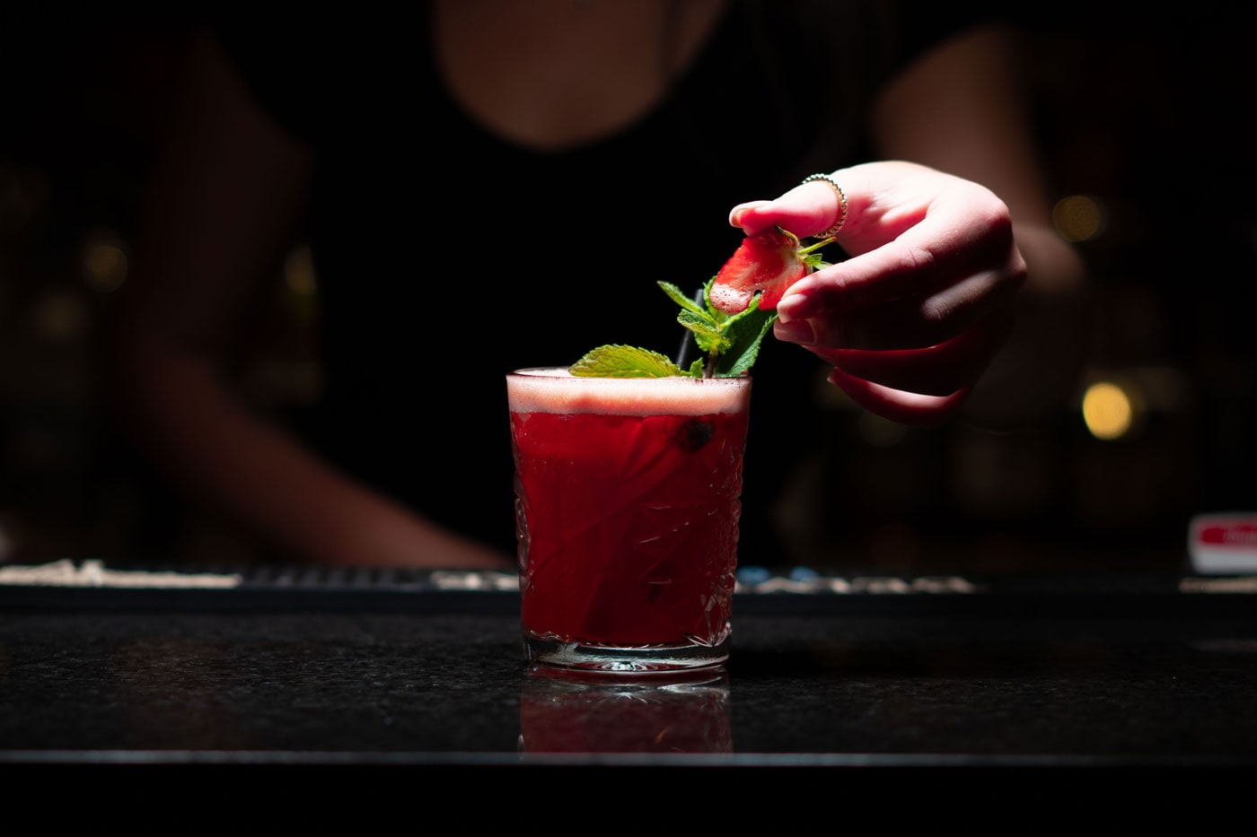 A bartender placing a flower garnish on a deep red cocktail