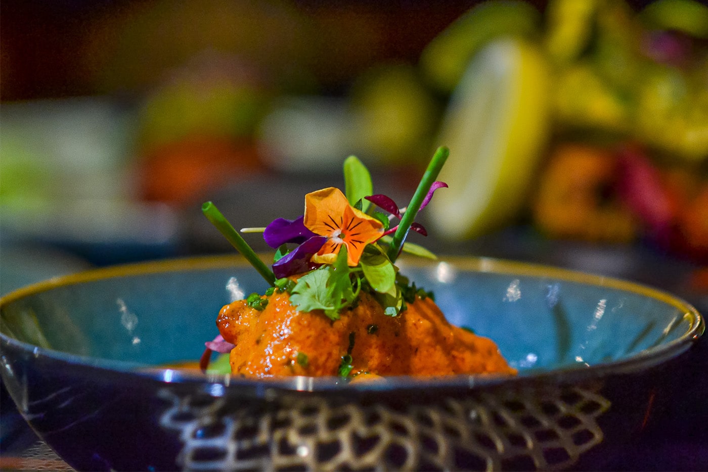 A spiced starter in a gold-rimmed blue bowl, finished with herbs and flowers